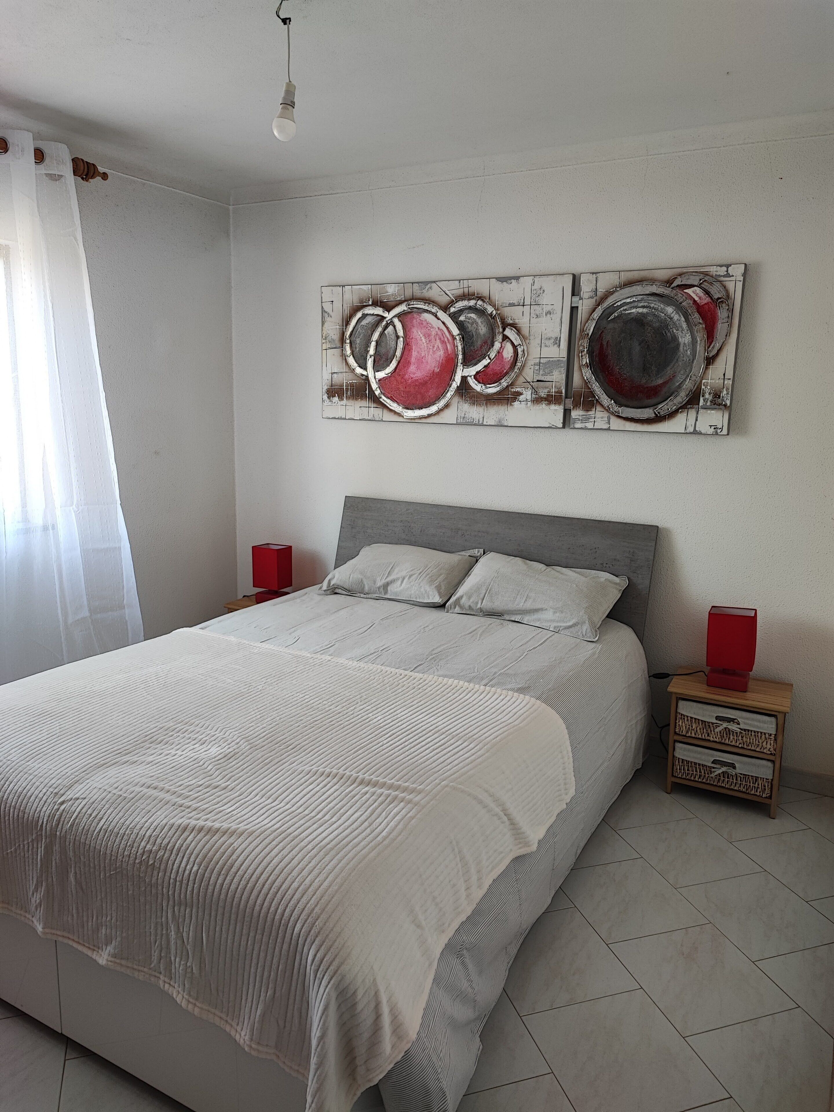 A bedroom with a bed, two wall art pieces, a nightstand, and a red lamp.