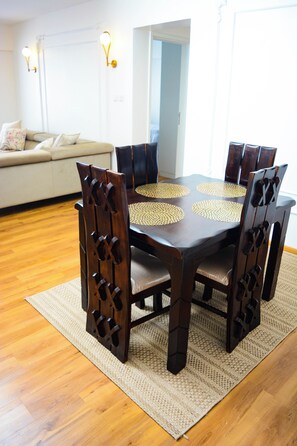 Een eettafel met een geweven placemat, omringd door houten stoelen met uitsnede patronen, op een geweven vloerkleed.