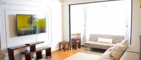 Una sala de estar con televisor, sofá y vistas amplias por un gran ventanal.