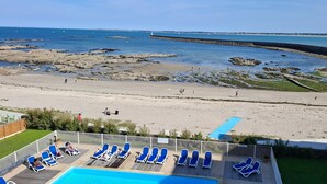 Blick auf einen Strand mit einem Poolbereich, Liegestühlen und einem Schild.