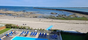 A beach view with a pool area featuring sun loungers and a sign. - Ocean-Colored Apartment with Pool and Beach Access (Le Croisic)