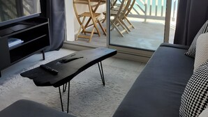Ein modernes Wohnzimmer mit Fernseher, einer Couch, einem Couchtisch und einem Balkon mit Meerblick.