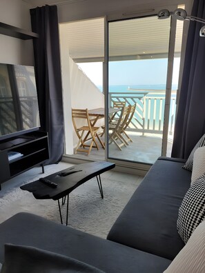 A modern living room with a television, a sofa, a coffee table, and a balcony with a view of the sea. - Ocean-Colored Apartment with Pool and Beach Access (Le Croisic)