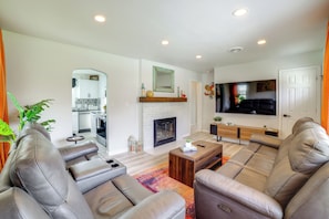 A modern living room with leather sofas, a fireplace, a TV, and a kitchen in the background.