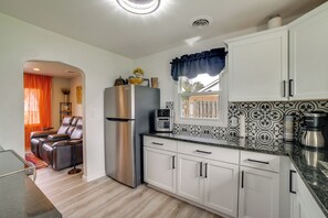 A modern kitchen with white cabinets, a stainless steel refrigerator, a coffee maker, and a window with a decorative valance.
