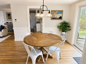 Een eethoek met een ronde houten tafel, witte stoelen, een hanglamp en een kamerplant.