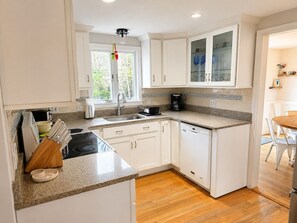 Een moderne keuken met witte kastjes, een granieten aanrechtblad, een koffiezetapparaat en een raam met uitzicht op groen.