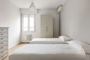 Un dormitorio con dos camas, un aparador, un radiador, una ventana y un equipo de aire acondicionado.