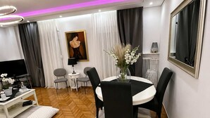 Een moderne woonkamer met een visgraat parketvloer, een ronde eettafel met stoelen, een televisie en een schilderij aan de muur.