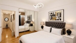 Een moderne slaapkamer met een groot bed, nachtkastjes, een spiegel en abstracte kunst aan de muur.