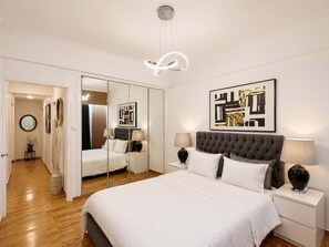 Ein modernes Schlafzimmer mit einem großen Bett, Nachttischen, einem Spiegel und abstrakter Kunst an der Wand.