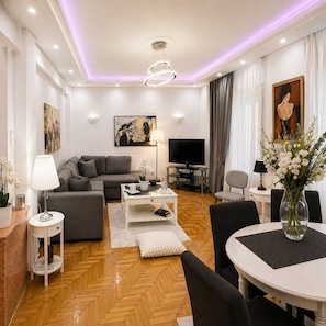 Ein modernes Wohnzimmer mit Sofa, Couchtisch, Fernseher und einem Essbereich mit Stühlen und Tisch.