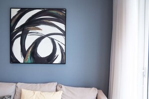 Ein Zimmer mit blauer Wand, einem beigen Sofa und einem großen abstrakten Gemälde.