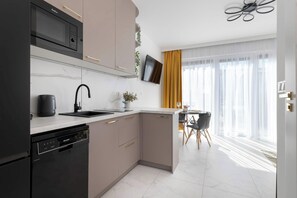 A modern kitchen with a dishwasher, microwave, and sink. There is a dining area with a table and chairs. - Two-level Apartment | Garden | Parking | Close to the Beach (Jastrzębia Góra)