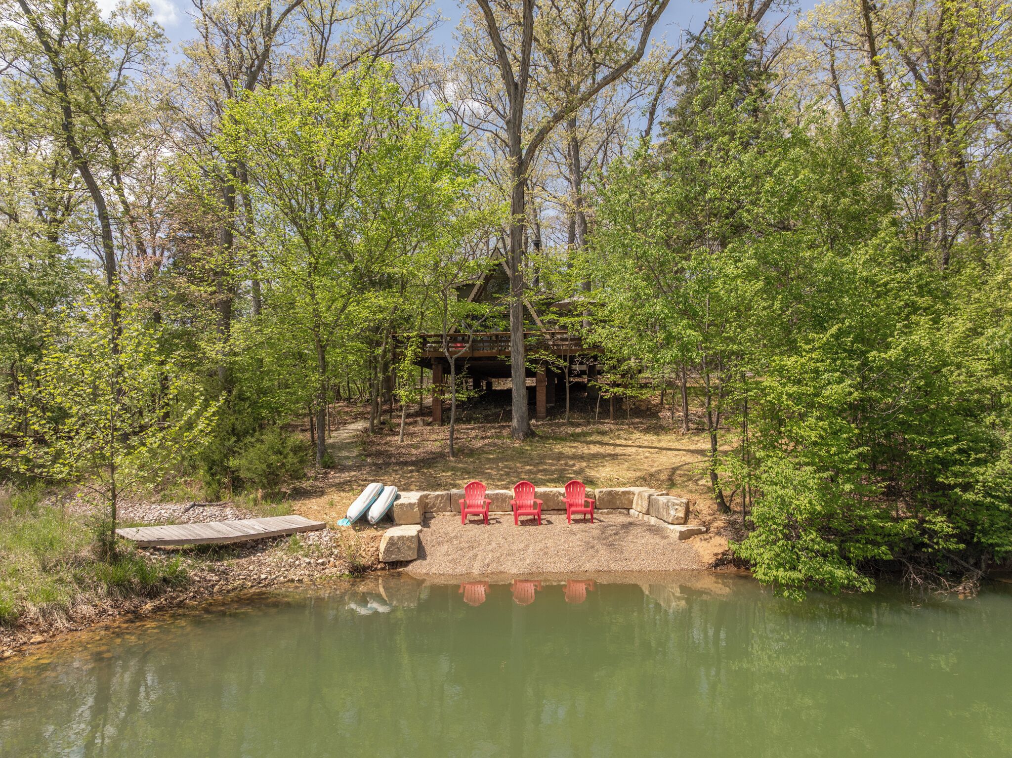 A rustic cabin with a dock, surrounded by trees and a pond.