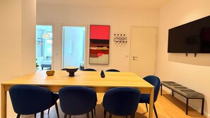 Un comedor moderno con una mesa de madera, sillas azules, un cuenco, un jarrón y un cuadro abstracto rojo.