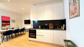 Una cocina moderna con armarios blancos, un comedor con sillas azules y un televisor de pantalla plana montado en la pared.