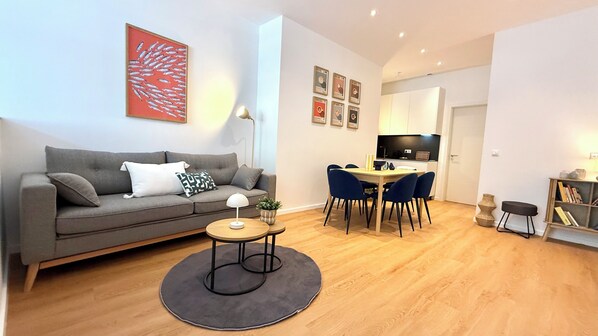 Una sala de estar moderna con un sofá gris, una mesa redonda de centro y un comedor con sillas y una mesa.