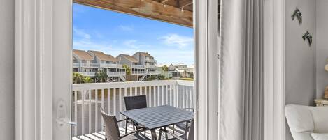 A balcony with a table and chairs, a white railing, and a view of a residential area.