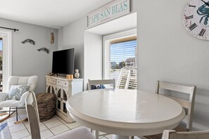 Ein Zimmer mit rundem Tisch, Stühlen, einem Fernseher, Wanddekoration und einem Fenster mit Jalousien.