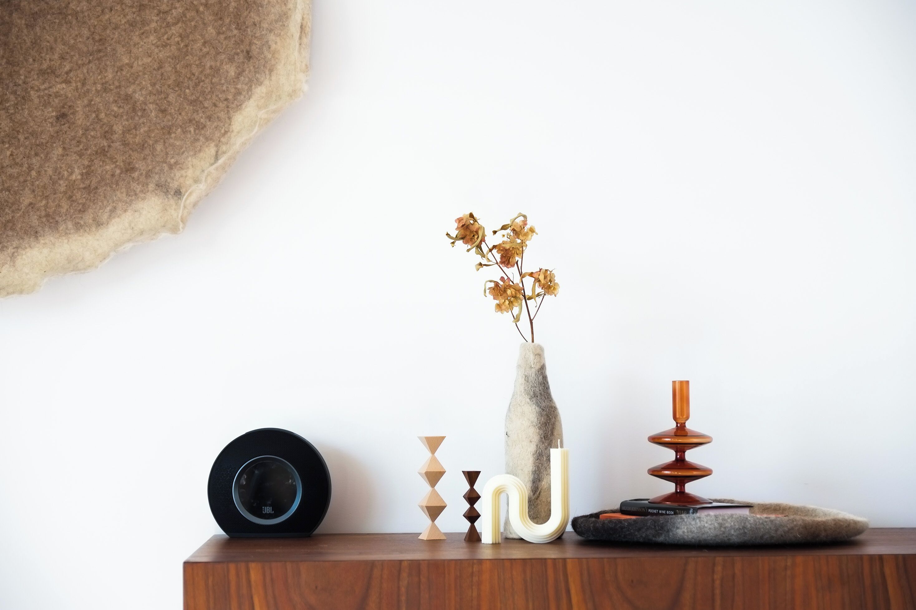 A wooden table with a black speaker, a vase with dried flowers, and geometric decorative items.