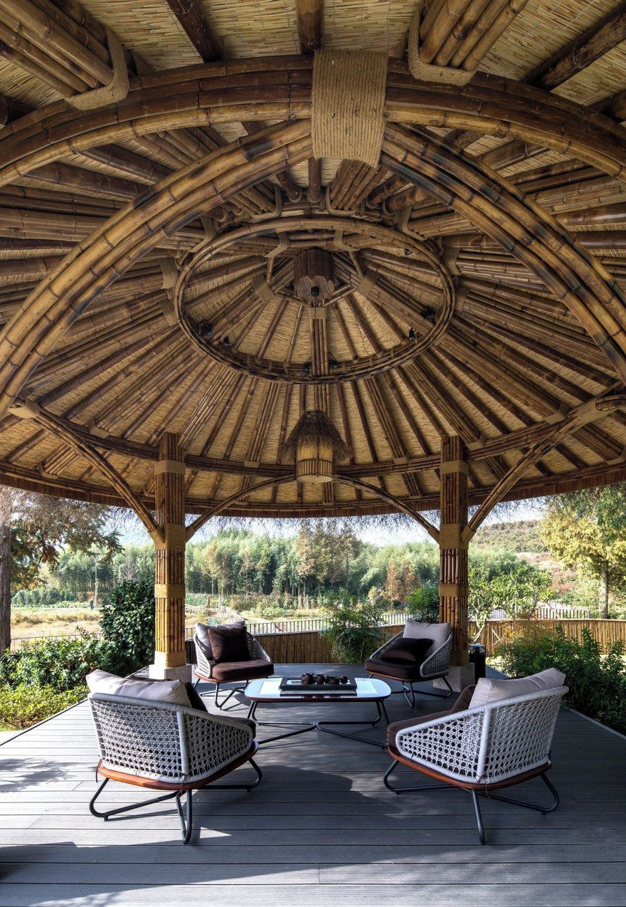 A covered outdoor area with a circular bamboo ceiling, two wicker chairs, and a small table.