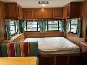 A compact RV interior with a bed, a bench, and a window seat.