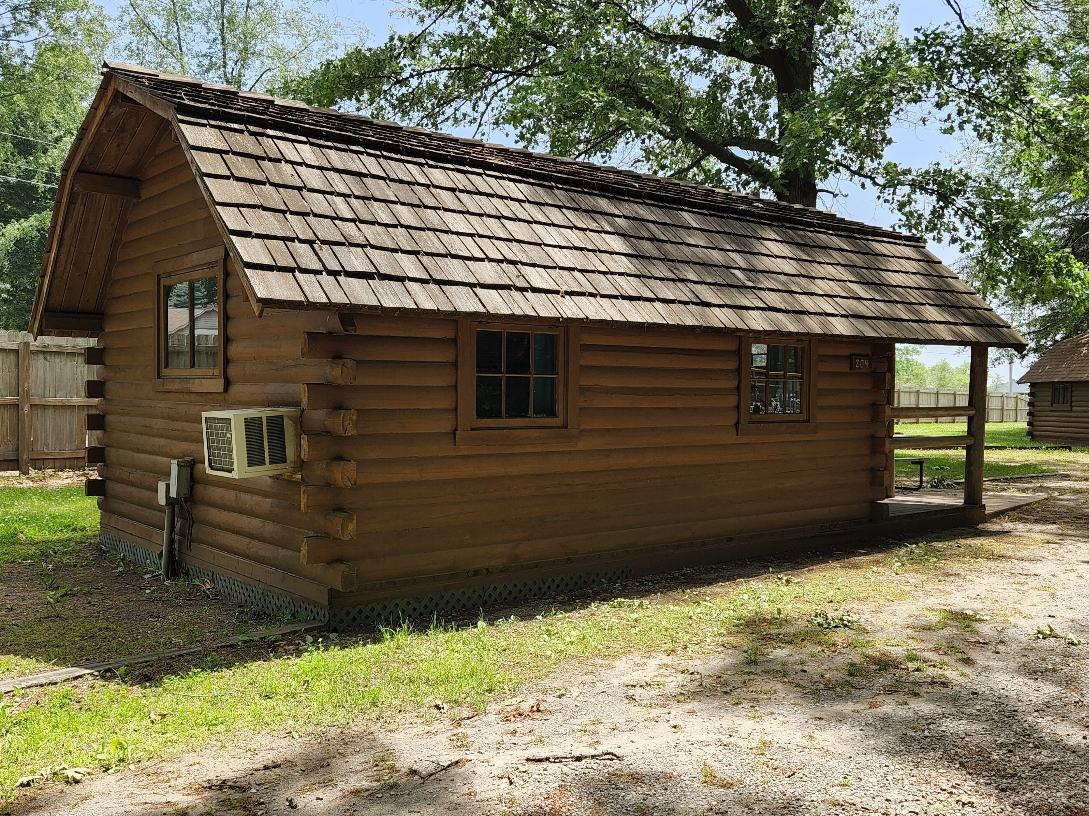 A wooden log cabin with a pitched roof, a small porch, and a window.