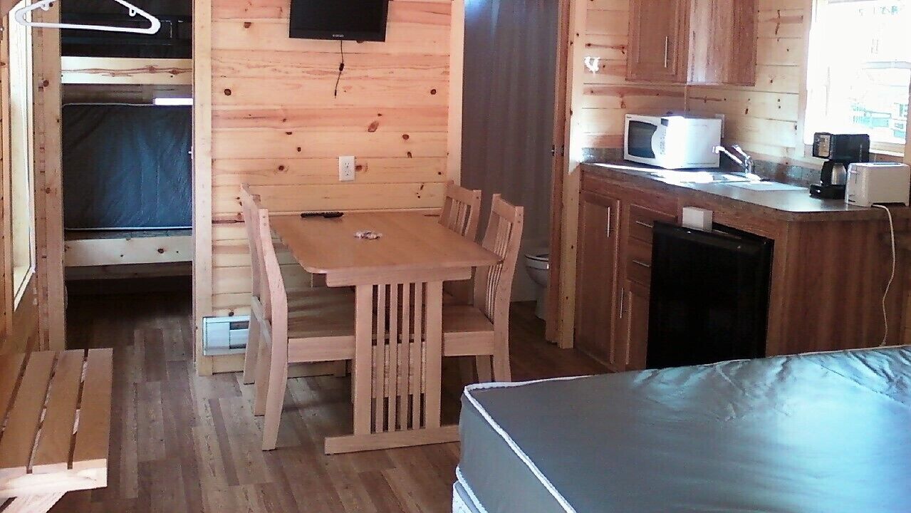 A compact cabin with a wooden interior, a dining area with a table and chairs, a kitchenette with a microwave, and a bed.