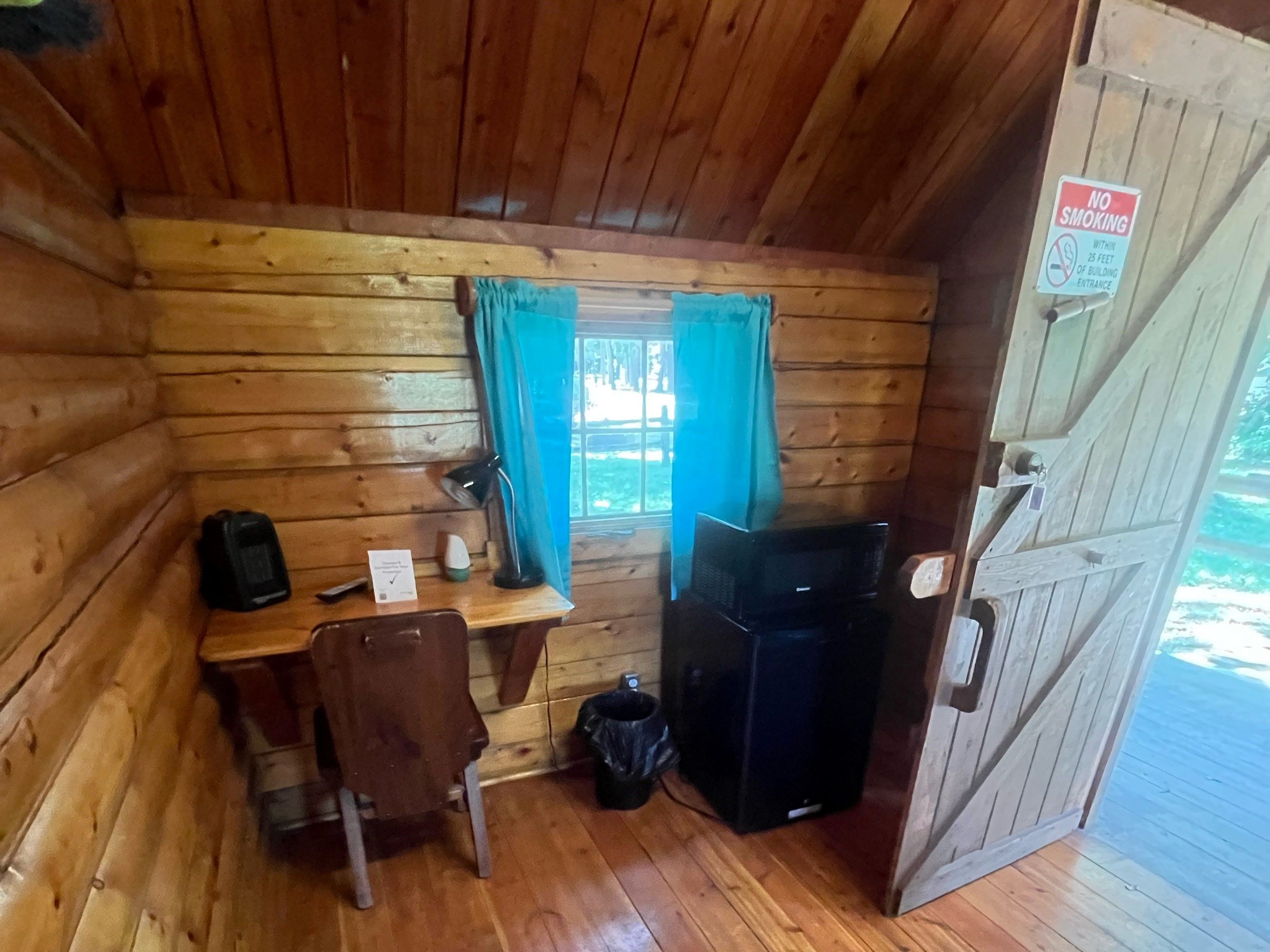 Una cabaña pequeña con interior de madera, un escritorio con silla, un televisor y una puerta con letrero de 'No fumar'.