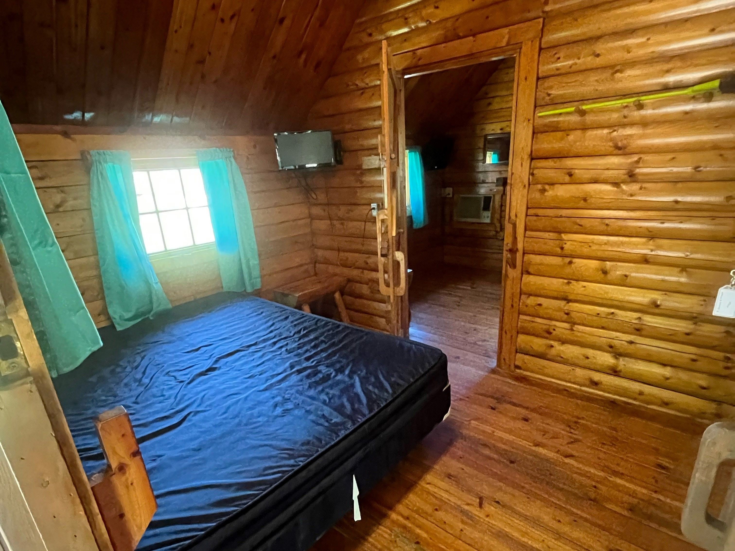Habitación de cabaña de madera con una cama, un televisor y un microondas al fondo.
