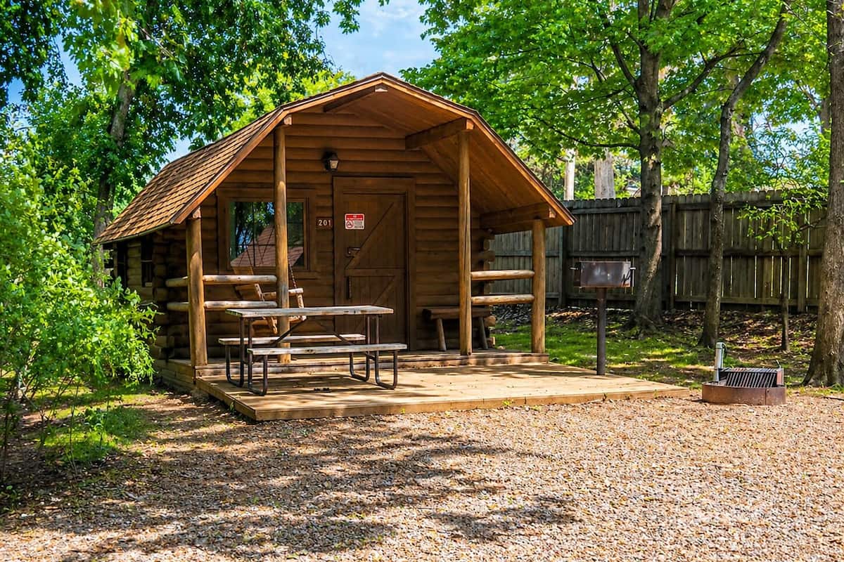 A wooden cabin with a porch, picnic tables, and a mailbox.
