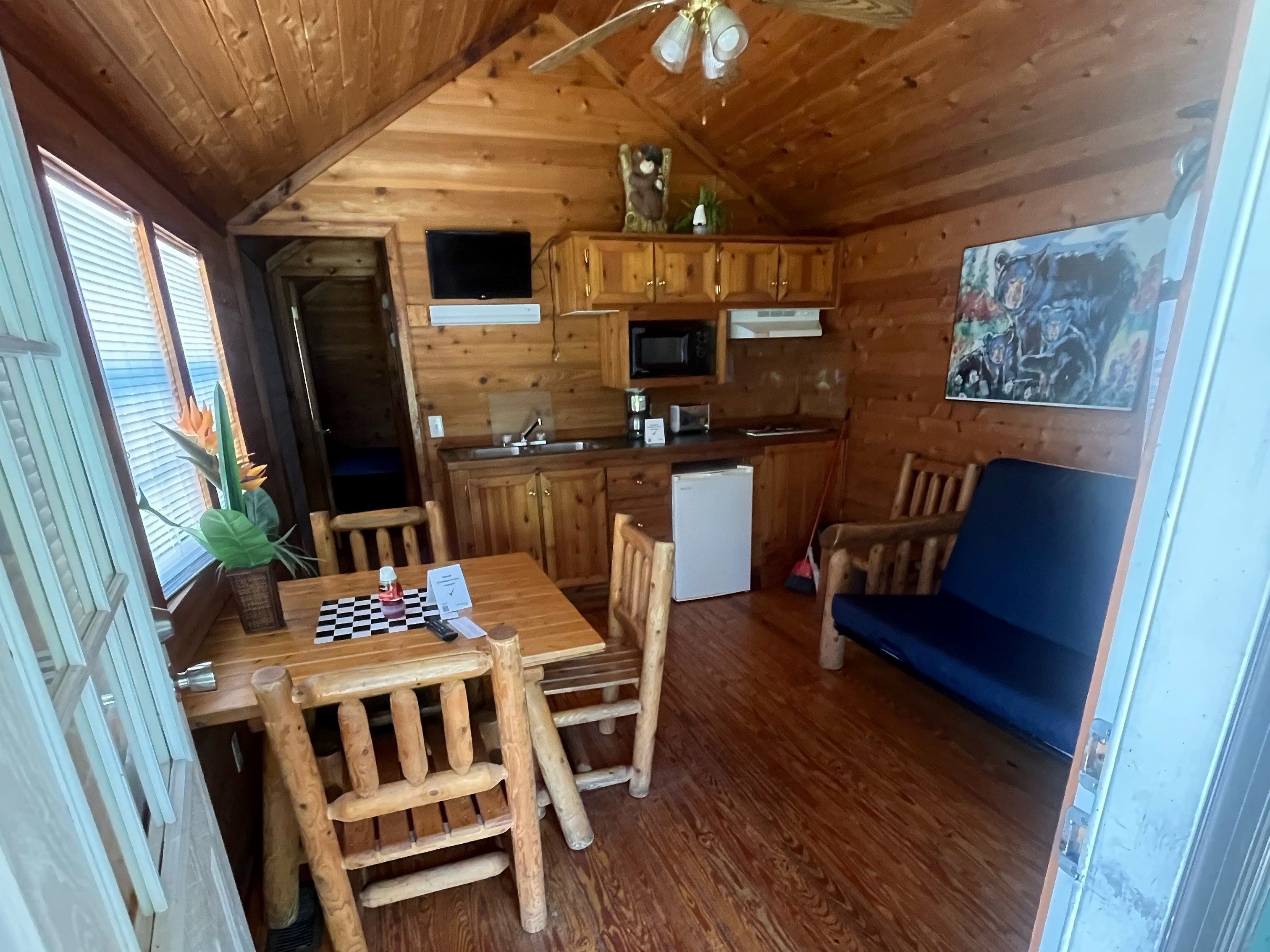 Ein Holzblock-Interieur mit Esstisch, Stühlen, einer kleinen Küchenzeile und einem blauen Sofa.