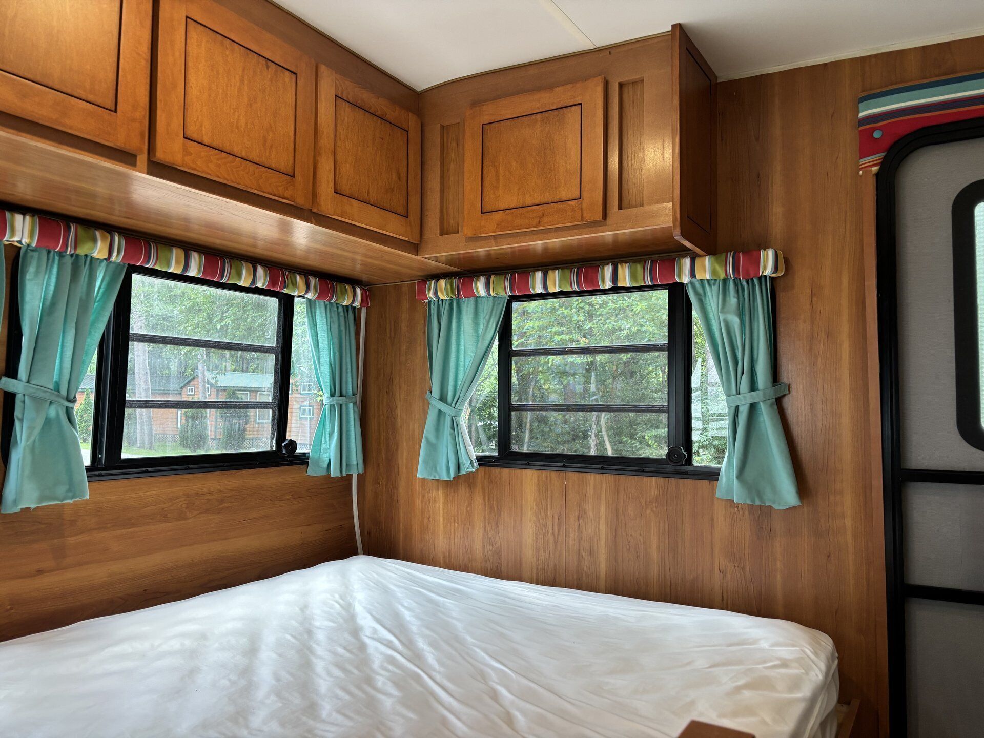 Un dormitorio con paredes de madera, una cama y dos ventanas con cortinas.