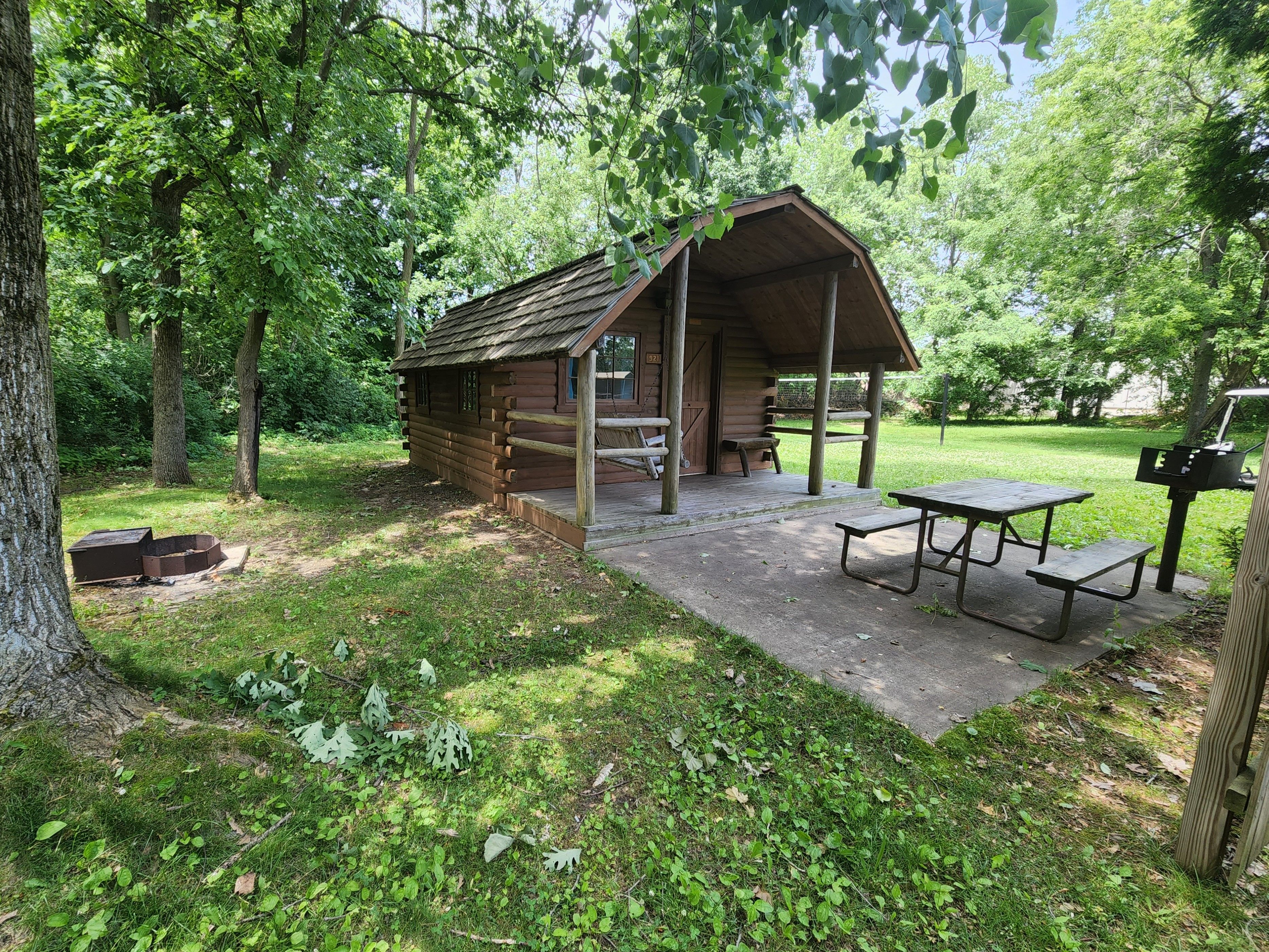 A rustic wooden cabin with a porch, picnic table, and grill area.