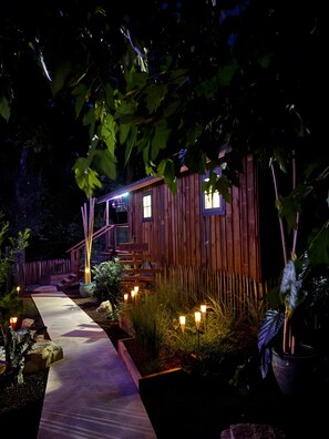 A wooden cabin with a wooden deck, a staircase, and a pathway leading to the entrance.