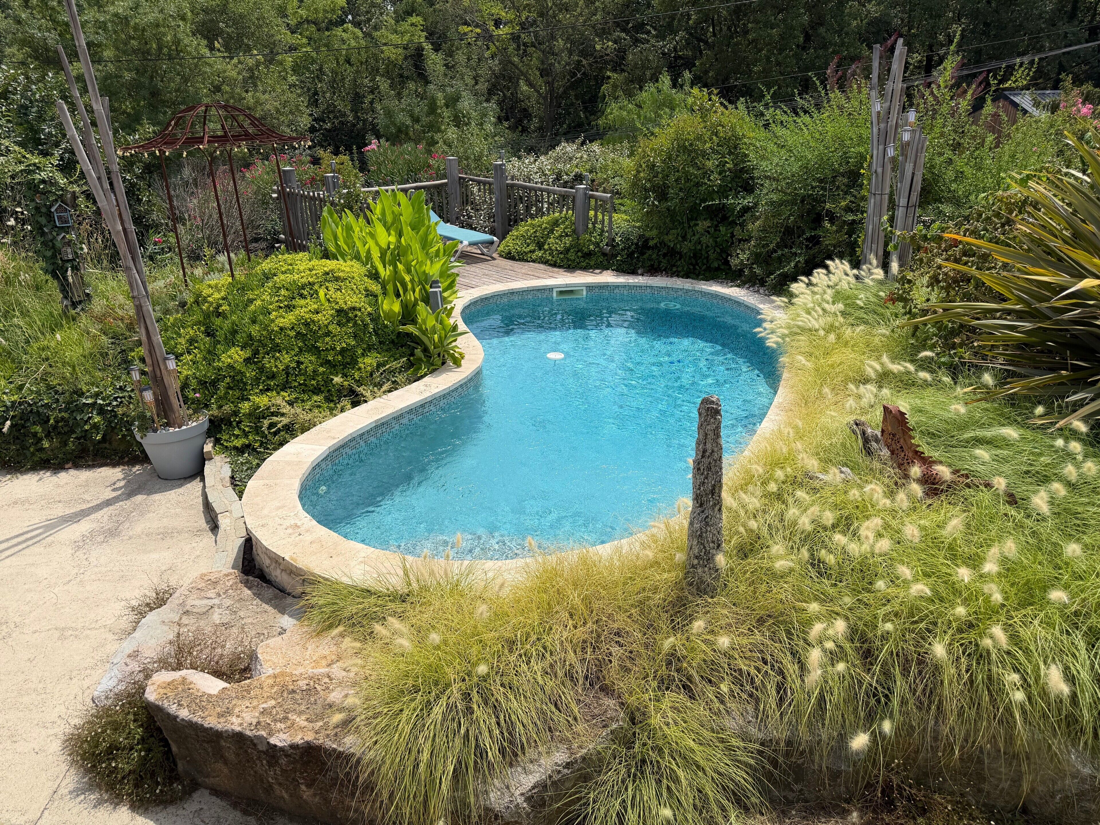Una piscina con cubierta de madera, rodeada de abundante vegetación y una valla de madera.