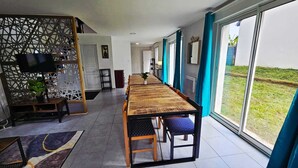 Un comedor moderno con una larga mesa de madera, sillas con acolchado azul y grandes ventanales con vistas al exterior.