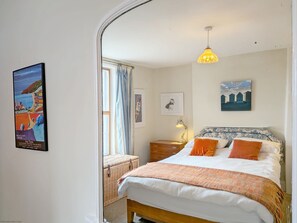 Ein Schlafzimmer mit Bett, Nachttisch, Lampe, einem gerahmten Bild und einem Fenster mit Vorhängen.