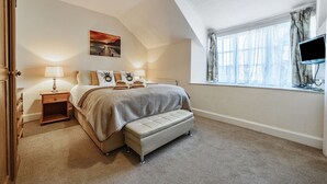 A bedroom with a bed, a nightstand, a bench, a painting, a window with curtains, and a television. - Ambleside Cottage with free private parking (Ambleside)