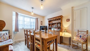 A dining area with a wooden table and chairs, a television, and a cabinet with glassware. - Ambleside Cottage with free private parking (Ambleside)