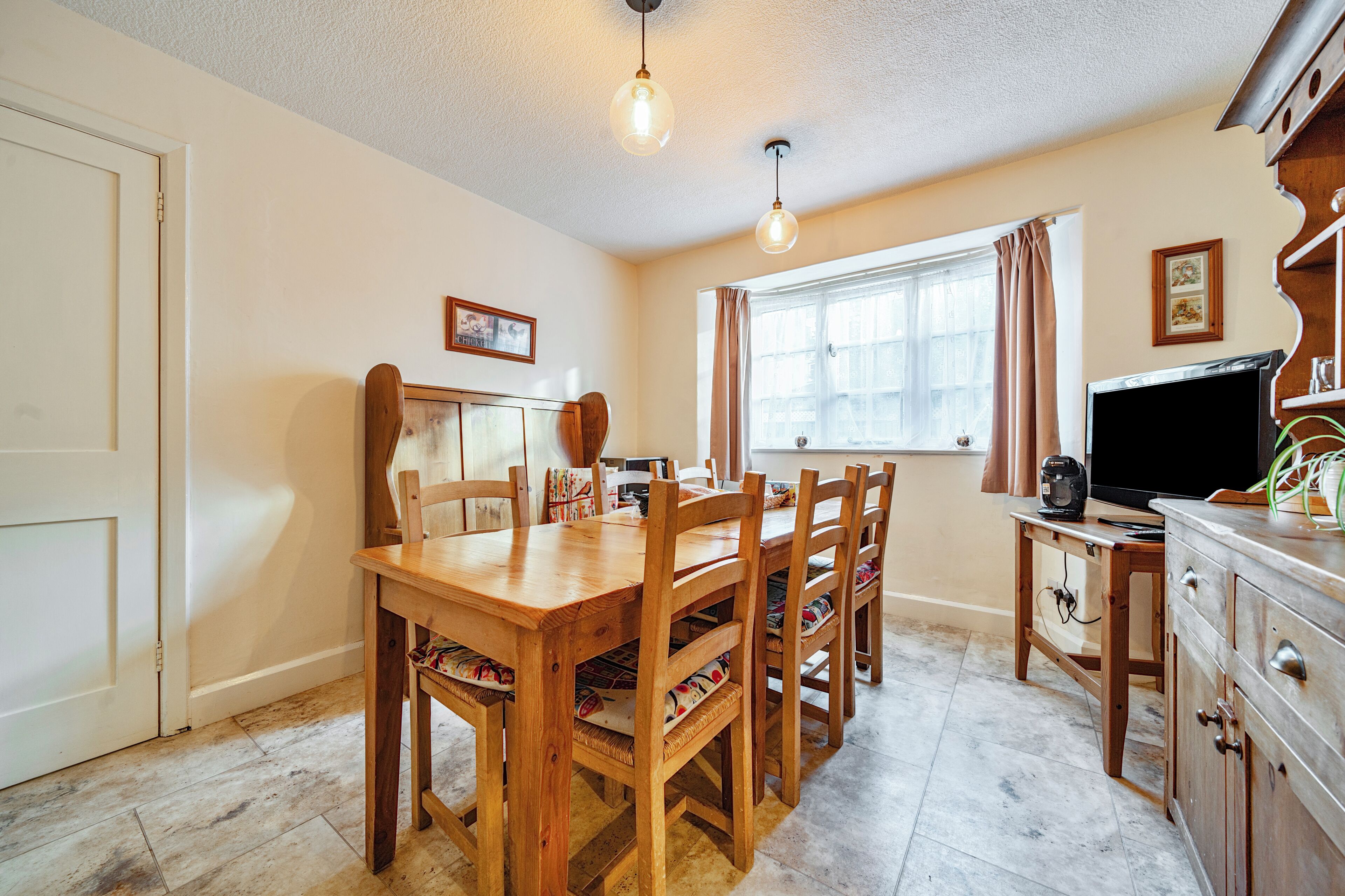 A dining area with a wooden table and chairs, a television on a stand, and a window with curtains.