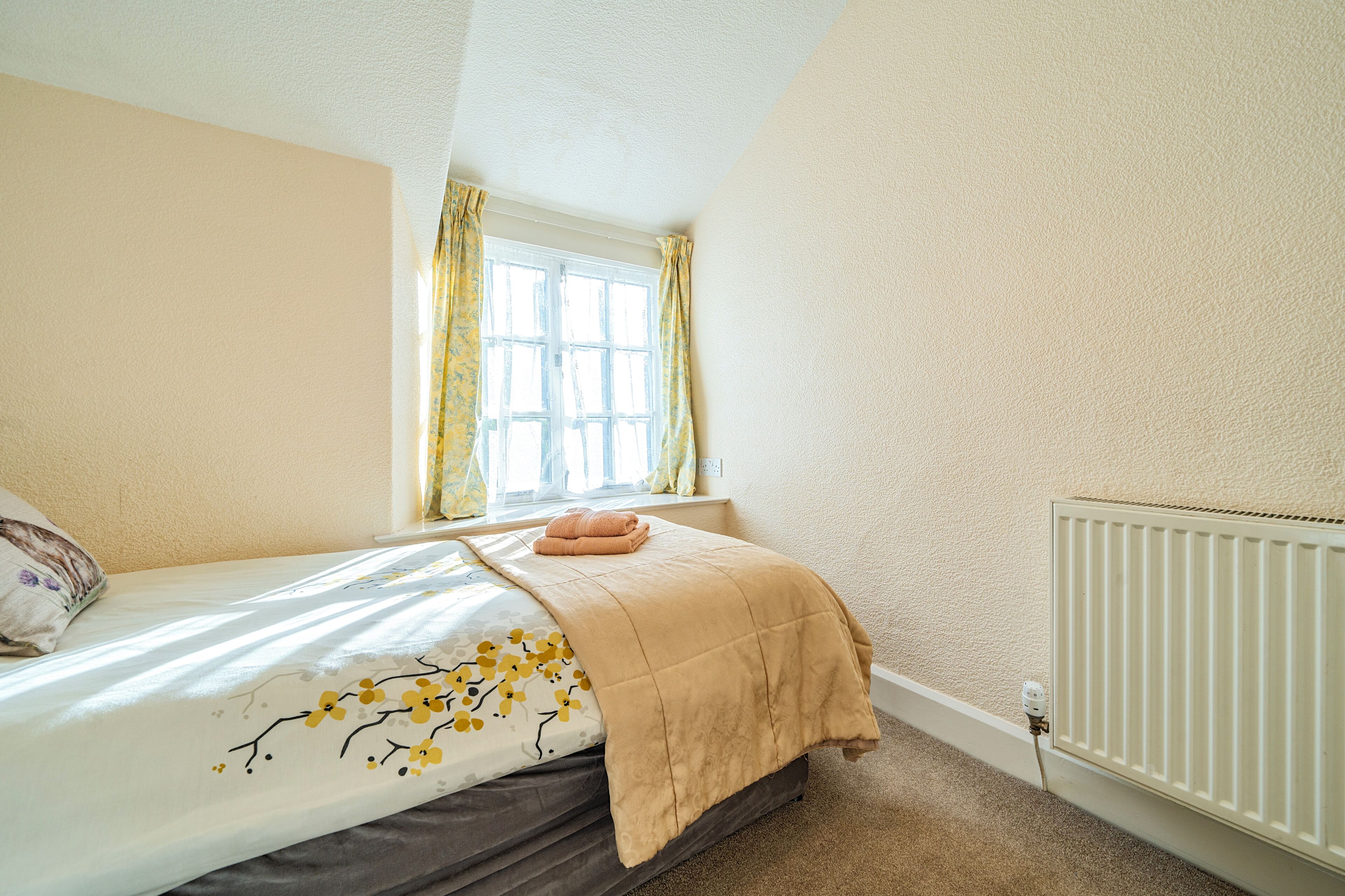Een slaapkamer met een bed, een raam met gordijnen, een radiator en een stopcontact.