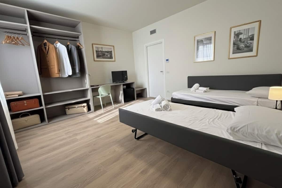 A hotel room with a bed, a desk, a chair, a wardrobe, and two framed pictures on the wall.
