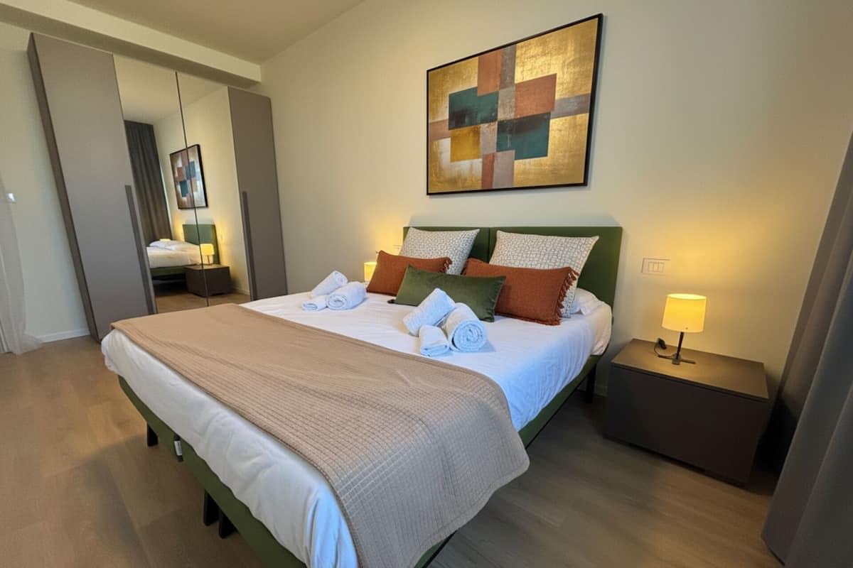 A hotel room with a bed, a nightstand, a lamp, a painting, and a mirror.