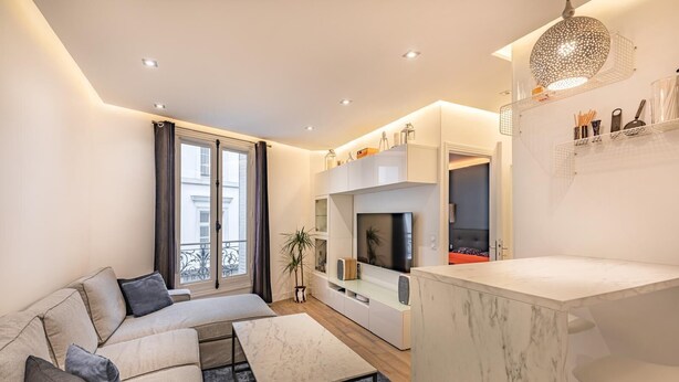 A modern living room with a sofa, TV, and a dining area with a marble table.