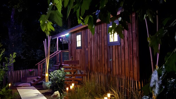 A wooden cabin with a porch, a staircase, and a pathway leading to the entrance.