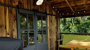 A wooden deck with a table and chairs, a barbecue grill, and a covered area with a door and windows.