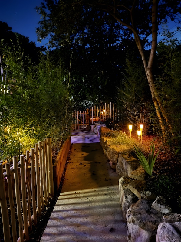 A nighttime pathway with wooden railings, a concrete path, and illuminated lights.