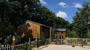 A wooden building with a metal roof, surrounded by a wooden fence and greenery.